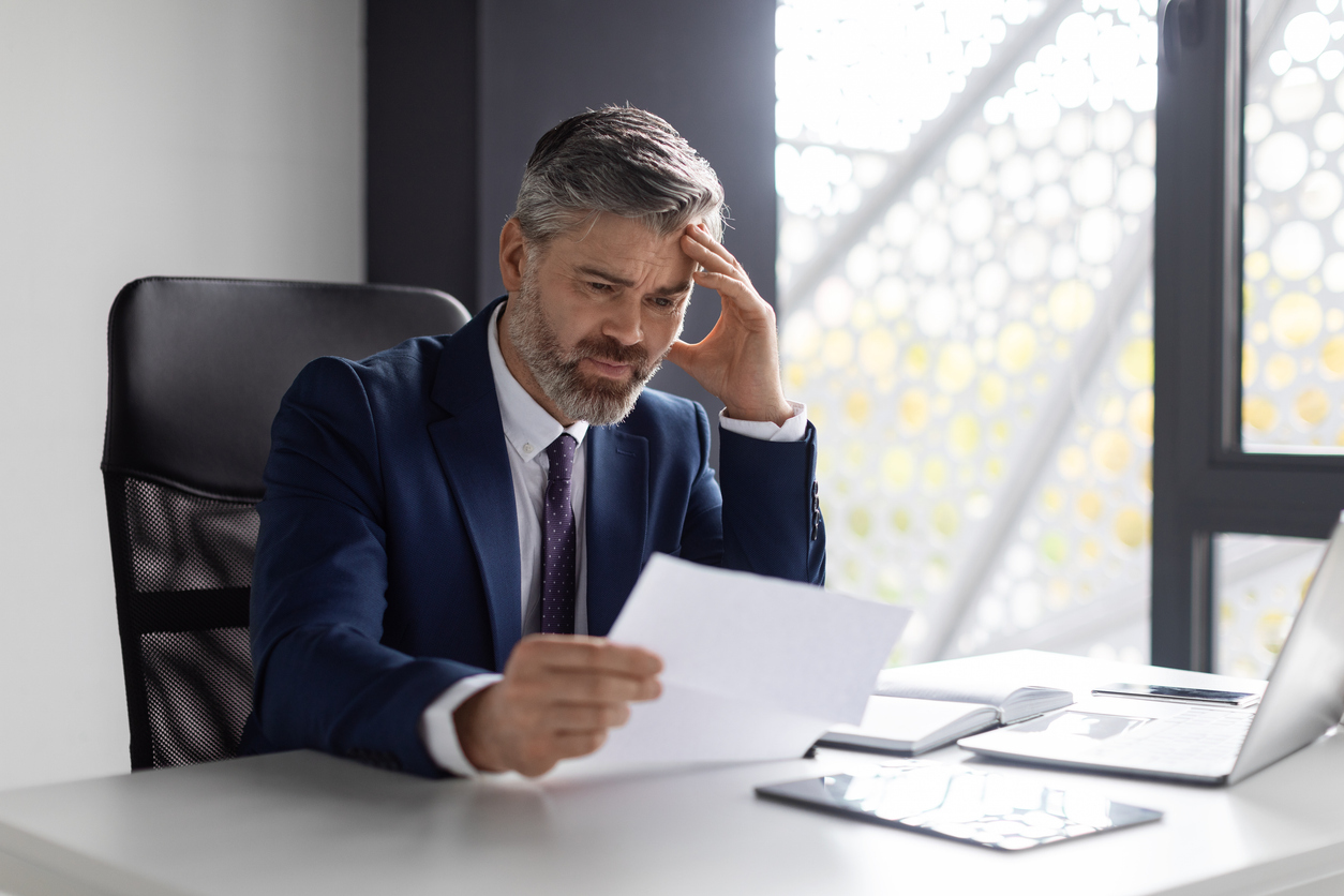 Un dirigeant d'entreprise penché sur son bureau regarde une feuille avec un air inquiet.